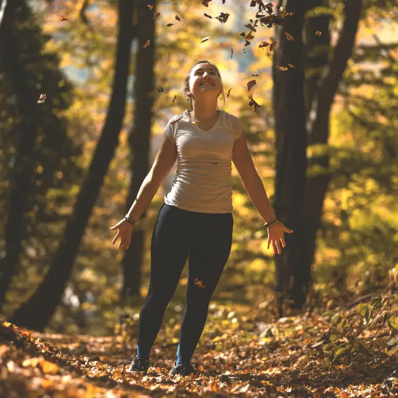 A young woman throwing leafs in the trees in autumn